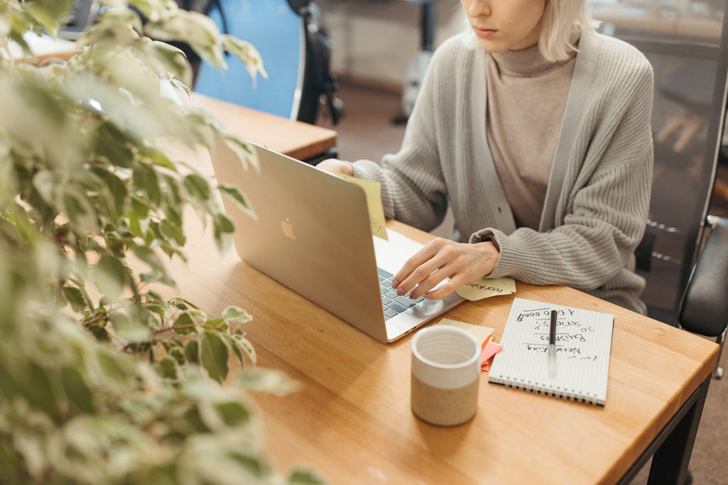 a girl at the laptop with coffee and notepad in the office