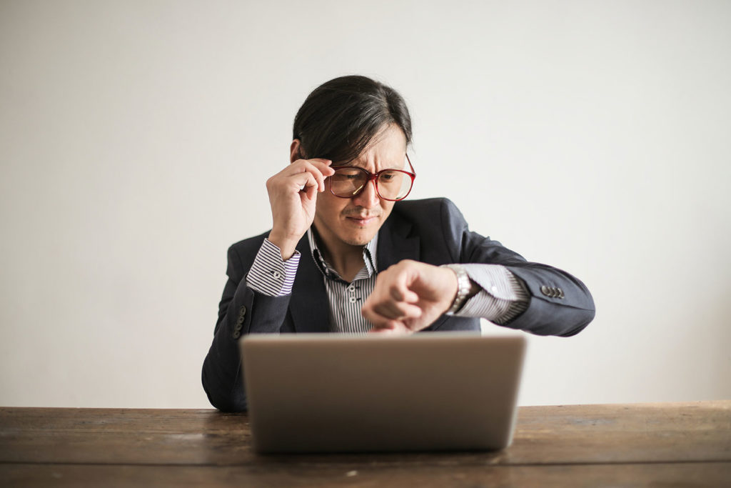 man with laptop checking time on his watch