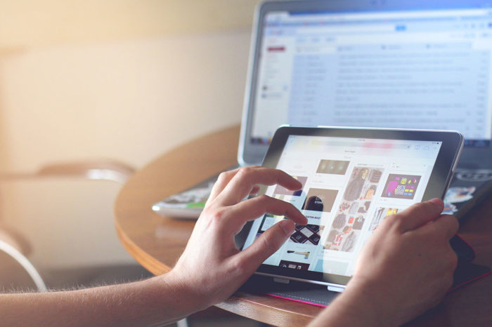 hand of a man holding tablet and browsing ads pinterest style laptop on bg